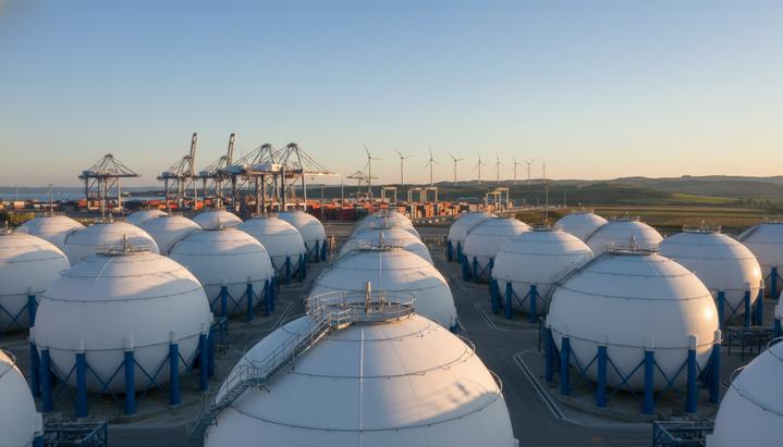 Современные сферические резервуары для хранения водорода в промышленном порту на фоне ветряных турбин и холмов.